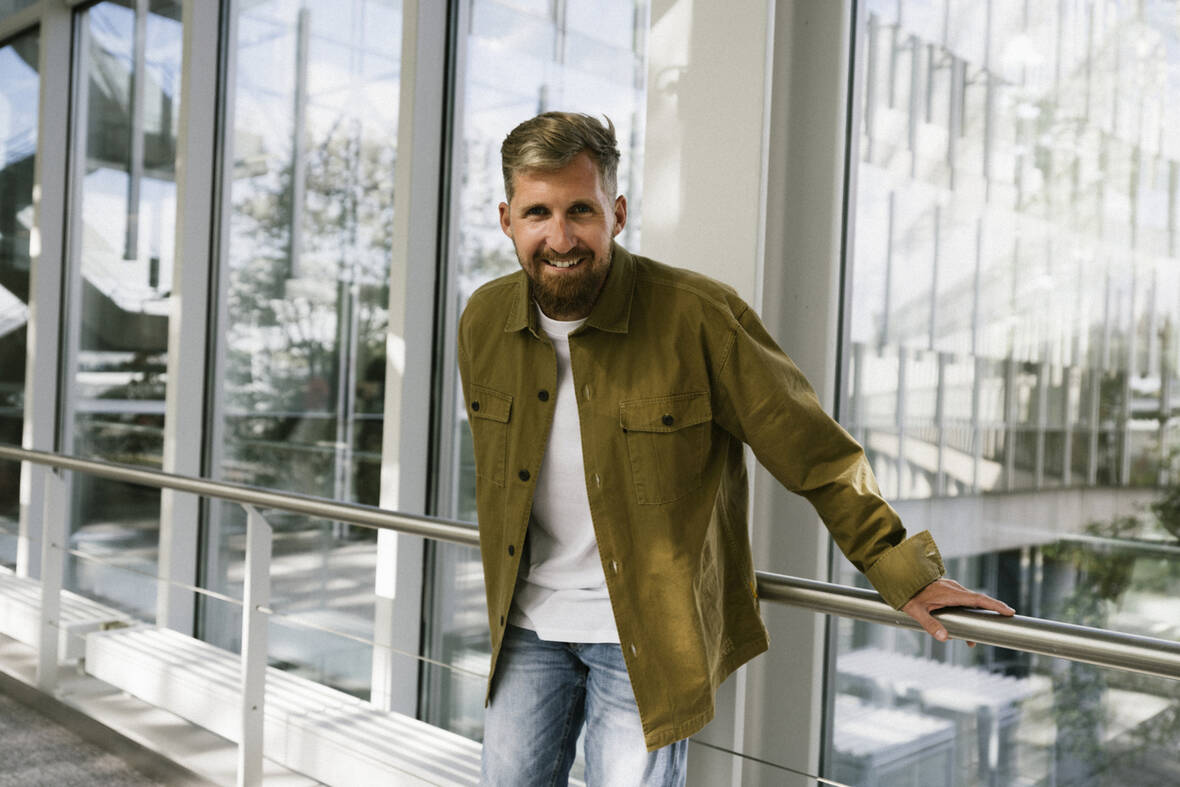 Unser Senior Product Owner steht lächelnd im Flur und hält sich am Geländer fest.