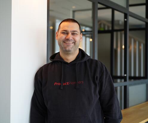 Ein Kollege aus Product Pioneers steht angelehnt an einer Säule und lächelt in die Kamera.