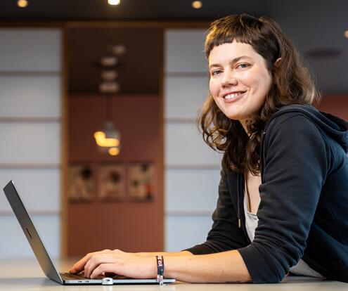 Softwareentwicklerin sitzt am Computer und guckt freundlich zur Seite in die Kamera.