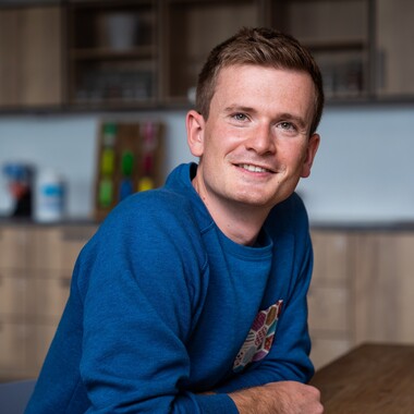 Unser Kollege Lead Product Manager Apps lehnt sich auf den Tisch Unser Kollege Lead Product Manager Apps sitzt an einem Tisch und lehnt sich nach vorne und blickt zur Kamera