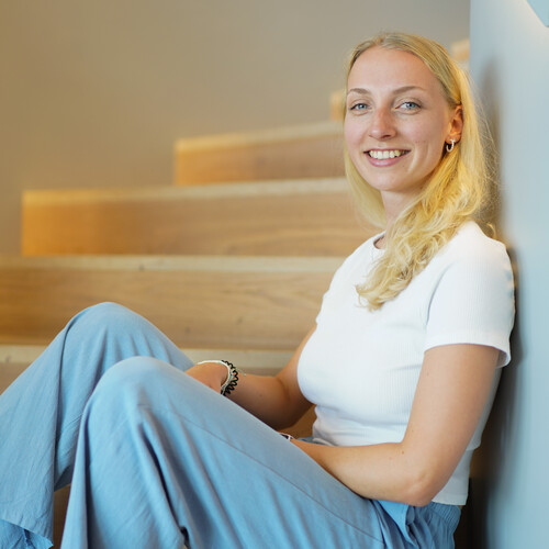 Eine Praktikantin sitzt auf einer Treppenstufe und lehnt sich an und lächelt in die Kamera.