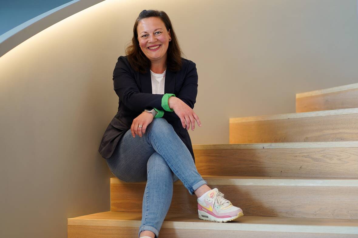 Technical Writerin Teil der ersten Staffel Role Models in Tech sitzt lächelnd auf Treppe. 