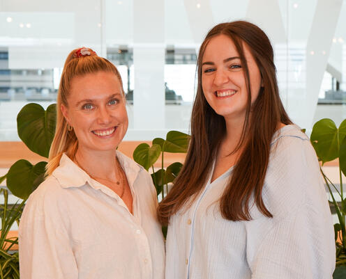 Unsere Recruiterinnen im Social Space Zwei Rekrutinnen aus einem Team stehen lächelnd vertraut im Social Space