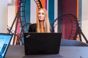 Kollegin aus dem E-Commerce sitzt vor ihrem Laptop und schaut aufmerksam zur Seite.