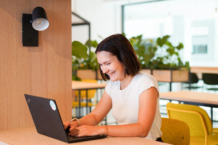Checkliste Bewerbung Kein Anschreiben nötig Das Bild zeigt eine junge Frau am modernen und freundlichen Otto Campus, die grinsend ihr Notebook bedient. Das Bild symbolisiert, dass für Bewerbungen bei OTTO kein Anschreiben nötig ist.