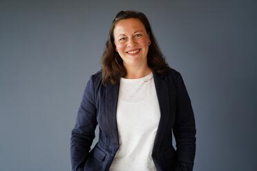 Technical Writerin bei OTTO steht vor einer blauen Wand und lächelt in die Kamera.