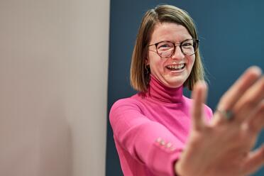 Eine Kollegin mit Brille und schulterlangen Haaren lächelt in die Kamera.