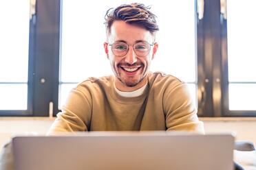 Ein Kollege aus dem UX Design schaut lächelnd auf seinen Laptop.